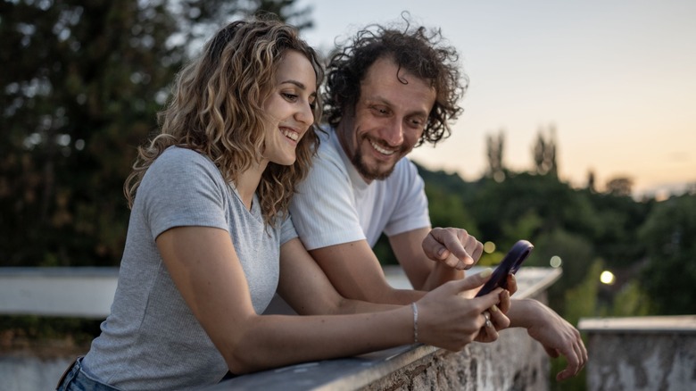 A man and woman smiling while looking at a phone