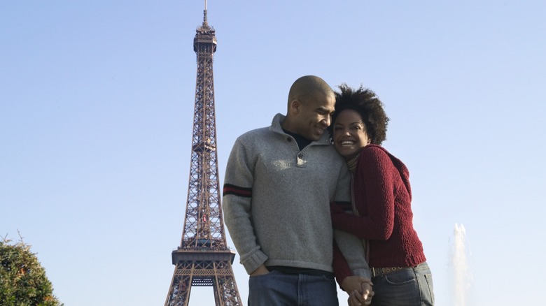 A couple smiling and posing in front of the Eiffel Tower