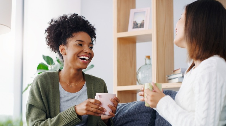 Two friends laughing while holding mugs