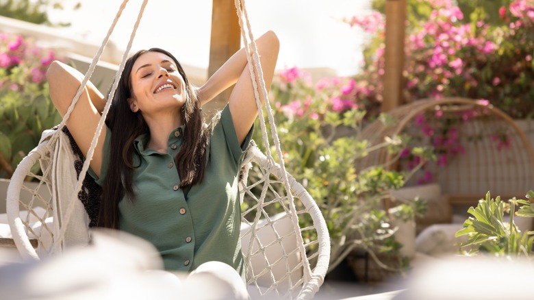 A woman sitting on a garden swing with her eyes clothes and smiling
