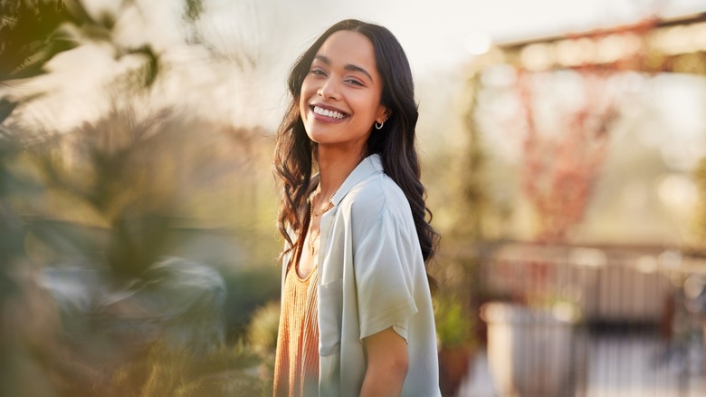 A woman smiling amid blurry foliage