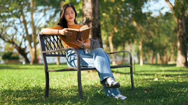 A woman sitting on a bench outdoors while reading a book