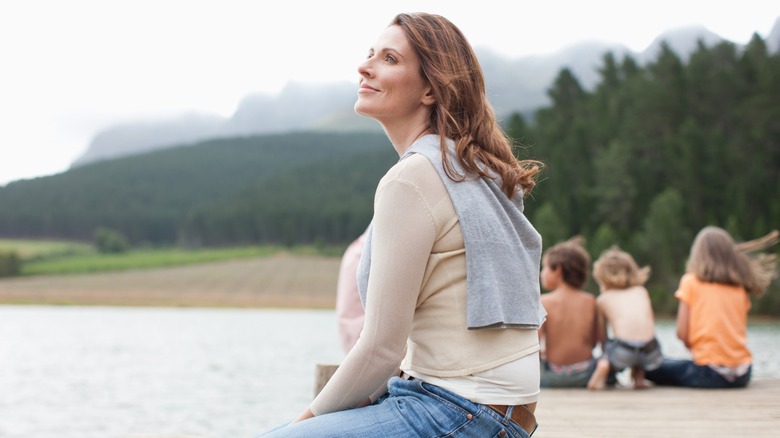 A woman sitting on a dock with children in the background
