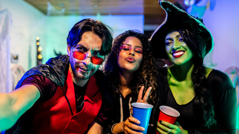 Three friends posing for a Halloween selfie, including a green witch and a vampire