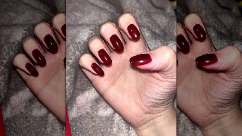 A semi-closed hand showing off a deep red nail polish with a gray blanket in the background