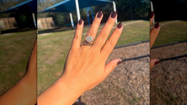 An open hand with a mown yard in the background showing a dark brown nail polish with a glossy finish