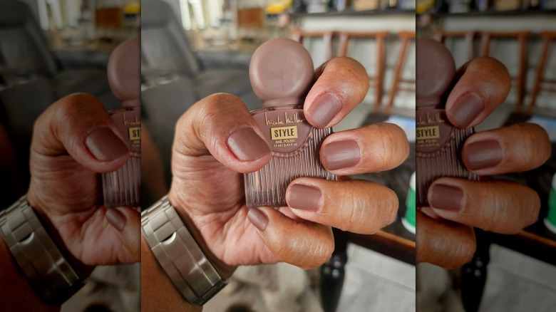 A hand holding a Nicole Miller nail polish bottle while showing off the corresponding light brown shade
