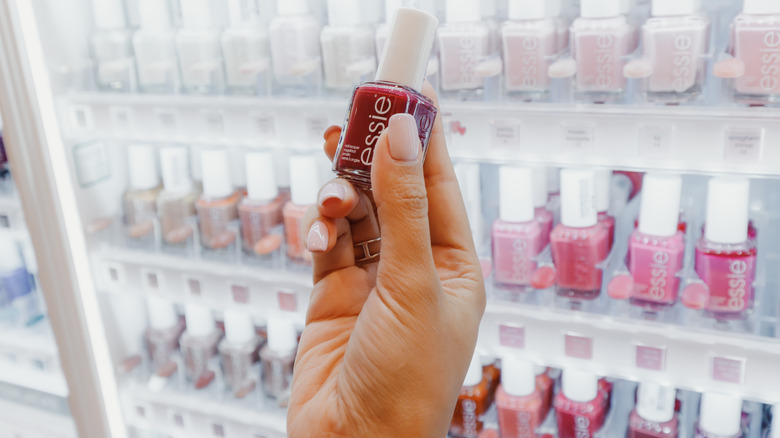 Hand holding Essie nail polish in front of rack of it