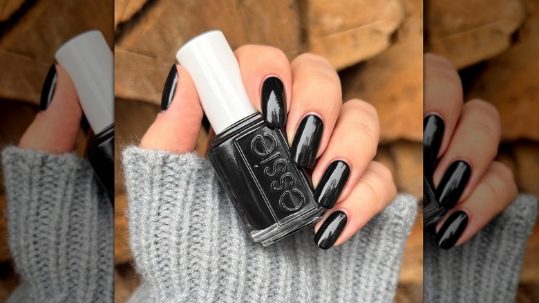 A close-up of a person's nails painted with Essie's Licorice and holding the nail polish bottle