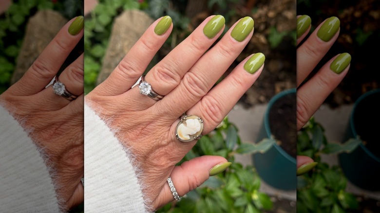 Open hand with various rings showing olive nail polish from Olive & June with potted plants in the background
