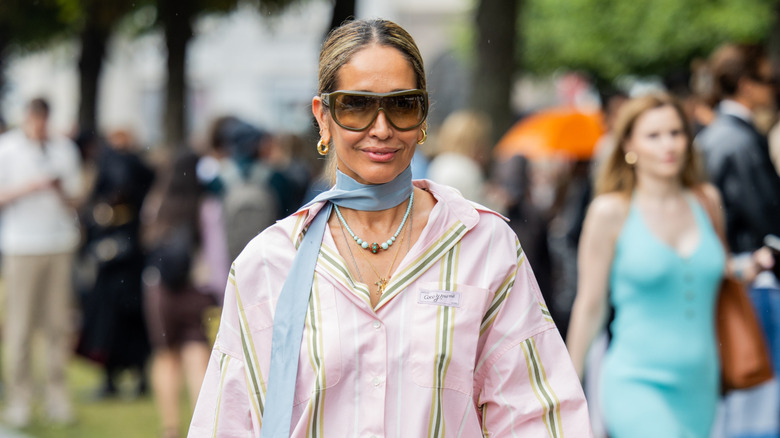 Tiany Kiriloff wears rose blouse, turquoise yellow fringed dress, blue bag, sunglasses outside