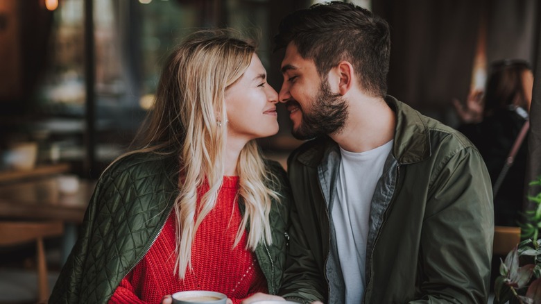 A younger couple rubbing noses while sitting at a table