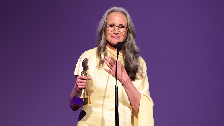 Andie McDowell on stage in a yellow gown accepting an award