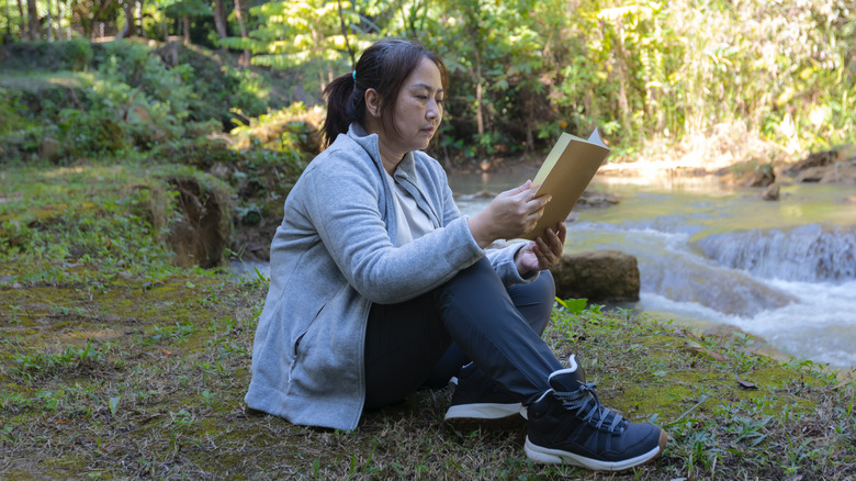 Woman reading in the woods near a stream