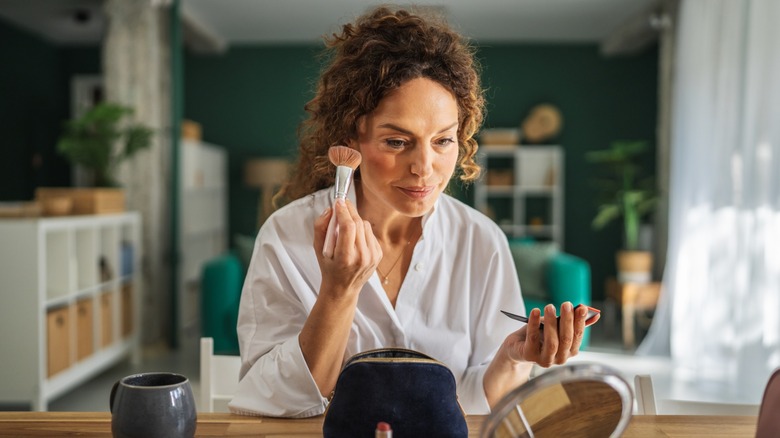 An older woman applying makeup at a desk