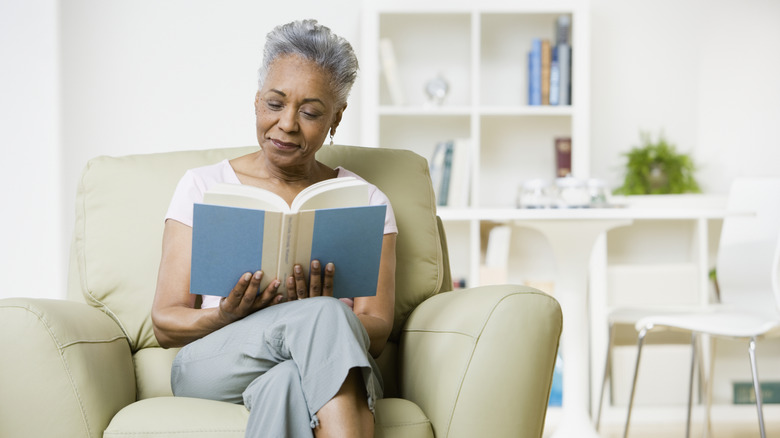 An elderly woman smiles as she reads a book