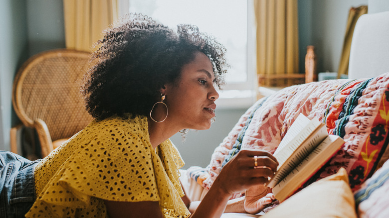 A woman laying on a couch and reading a book