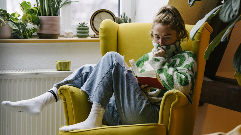 A woman sitting in a yellow armchair and reading a book