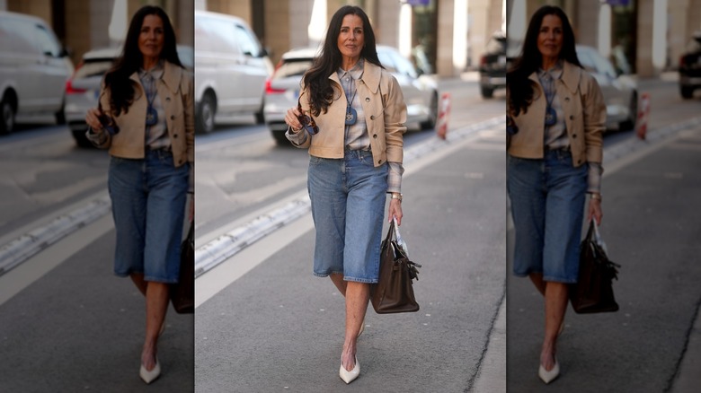 A woman walking in the street in long denim shorts and a beige jacket