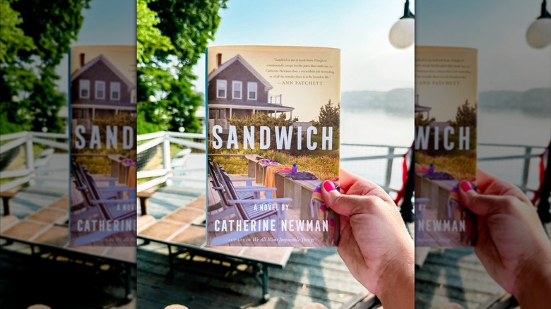 A hand holding up a copy of the book "Sandwich" in front of a harbor