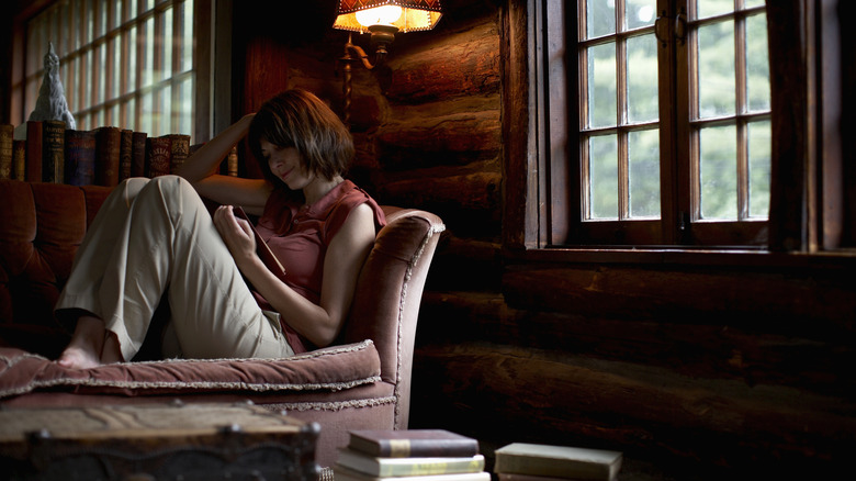 A woman sits comfortably on her couch and reads a book