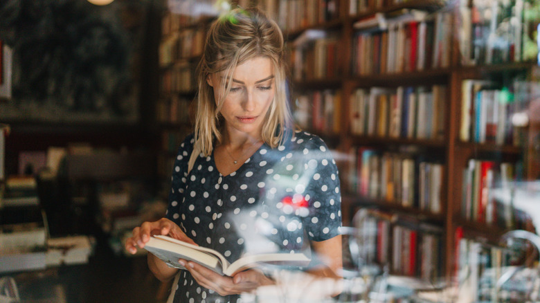 A woman in a blue polka dot dress reading a book in a bookstore through a window
