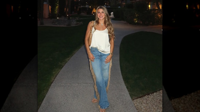 A woman outside at dusk wearing fringe jeans and a white tank top