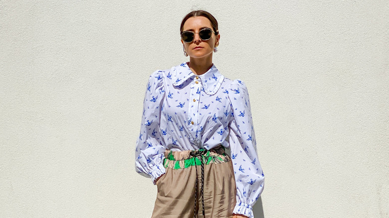 A woman with a peter pan collar and flowers on her shirt with beige pants and sunglasses