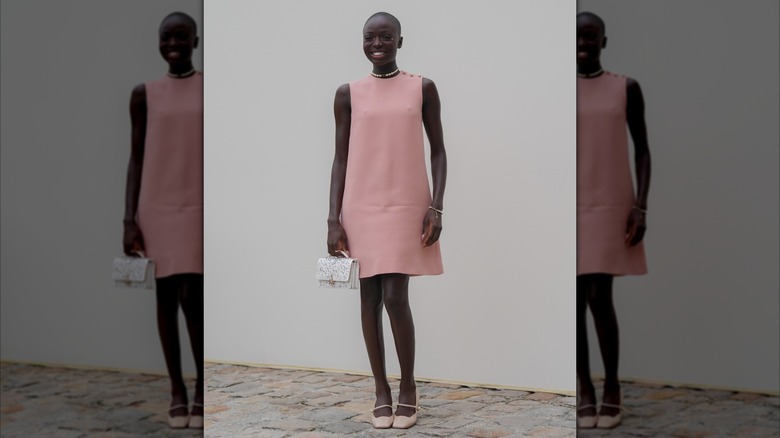 A woman wearing a dusty rose shift dress with a white bag and rose Mary Jane shoes