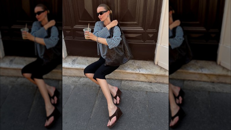 A woman sitting on a stoop wearing wedges and black capris with a striped shirt