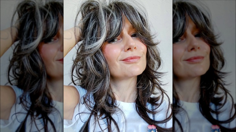 A woman with long layers and bangs with grey hair