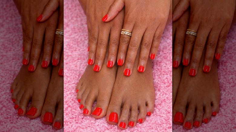 Hands and feet against a pink throw showing a bright red mani-pedi
