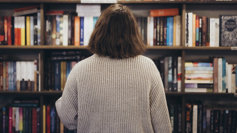 Young brunette woman choosing a book in a bookstore, back view