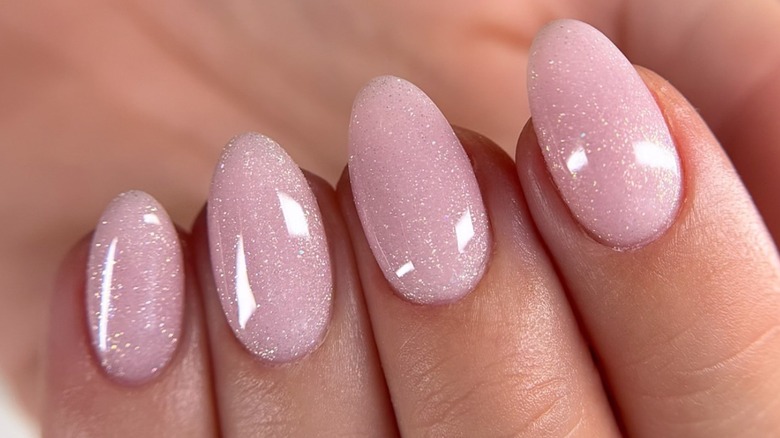 Fingers on a hand with cool toned skin with a sparkly, frosty pink manicure