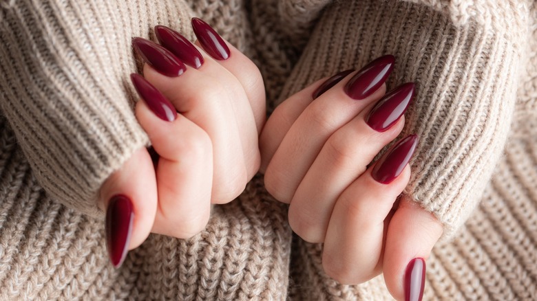 Two hands with a long cherry manicure on a person wearing a beige sweater