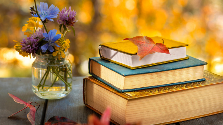 Stack of three various-sized books styled around fall leaves and next to a jar of flowers