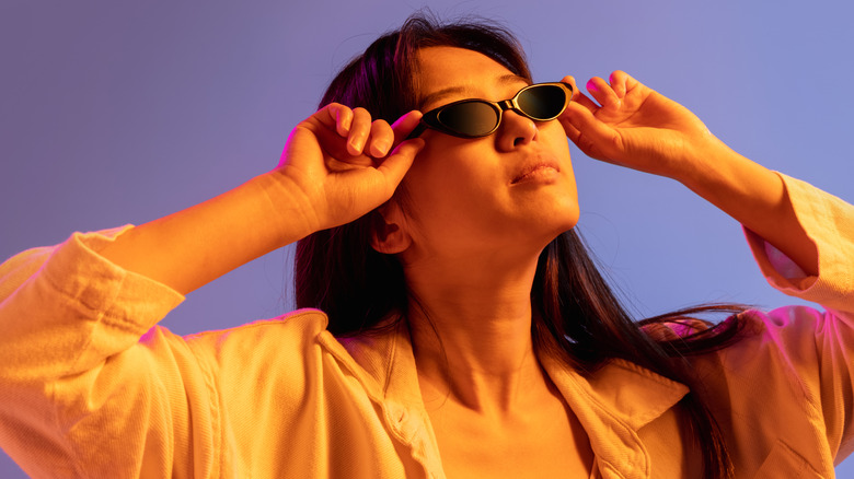 Woman wearing micro sunglasses against a purple background