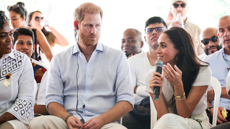 Prince Harry and Meghan Markle at an event with her holding a microphone