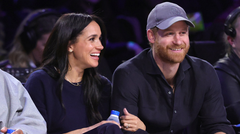 Prince Harry and Meghan Markle smiling and sitting courtside at a game