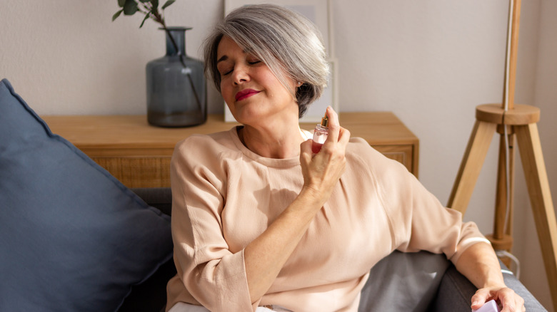 Older woman spraying perfume on the couch