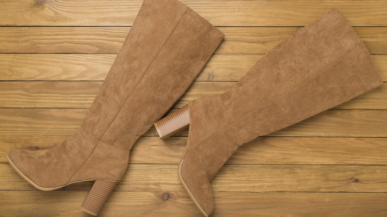 Brown suede boots laying down on a wooden floor
