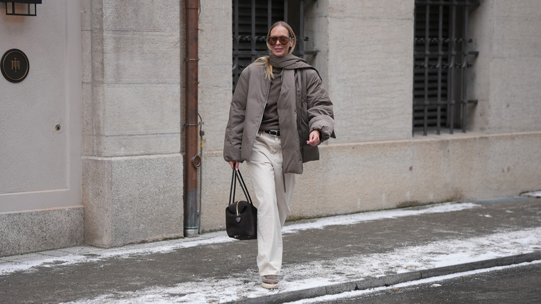 Mirja Klein is seen wearing a khaki padded jacket with an integrated scarf detail, a relaxed oversized silhouette and dropped shoulders from Arket; a brown cashmere knit sweater with a fine texture and classic crew neckline from Jacquemus; off white straight leg jeans with a high rise