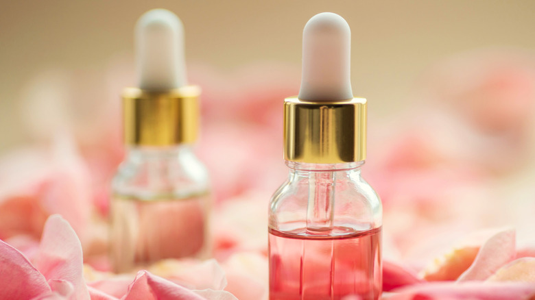 Two glass bottles of cuticle oil surrounded by pink flower petals