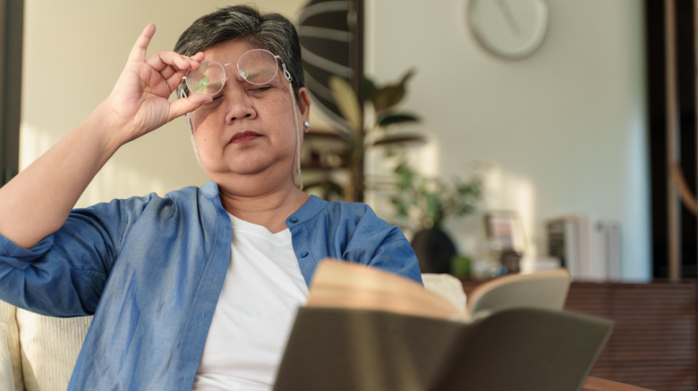 Older woman holding book, lifting glasses and squinting