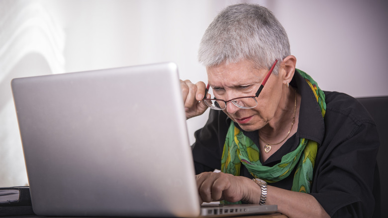 A woman with short hair and glasses using a laptop and squinting