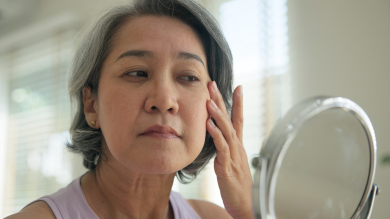 An older woman looking at her skin in the mirror