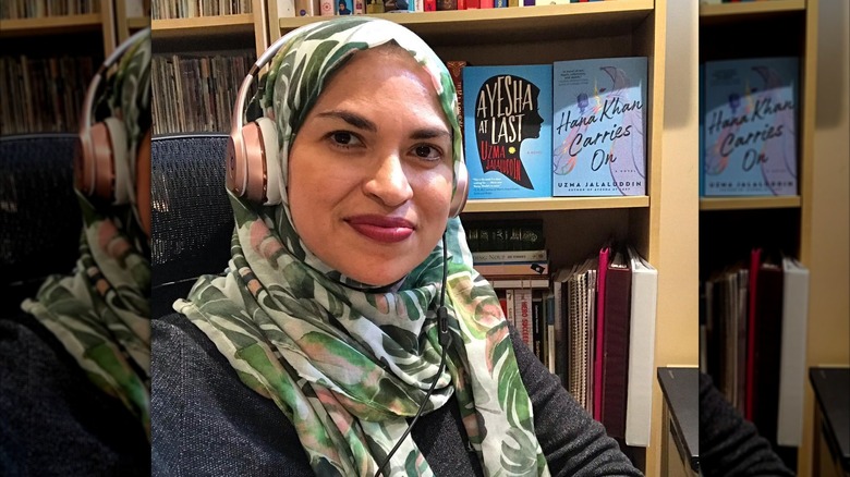 Uzma Jalaluddin posing for a selfie with her books "Ayesha at Last" and "Hana Khan Carries On" on the shelf behind her