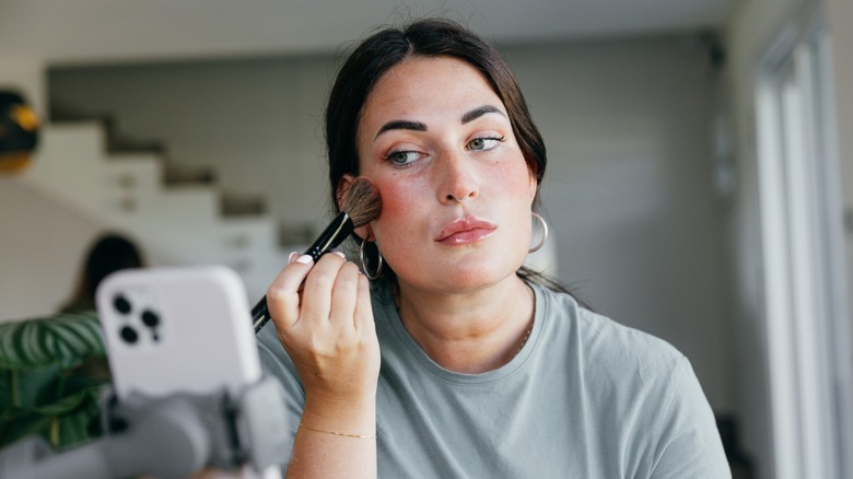 A woman applying blush to her cheek using a brush