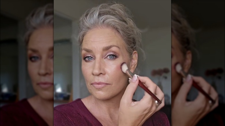 A woman blending blush high on her cheek using a small brush