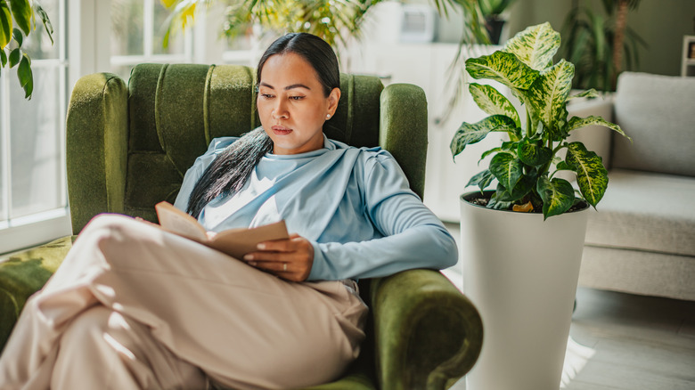 A woman reading a book as she sits comfortably on a green chair